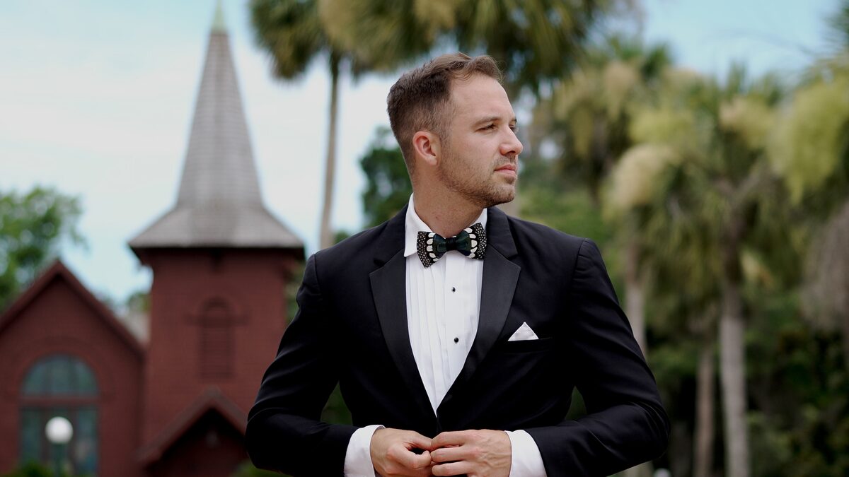 Groom buttoning his jacket in front of a red brick chapel