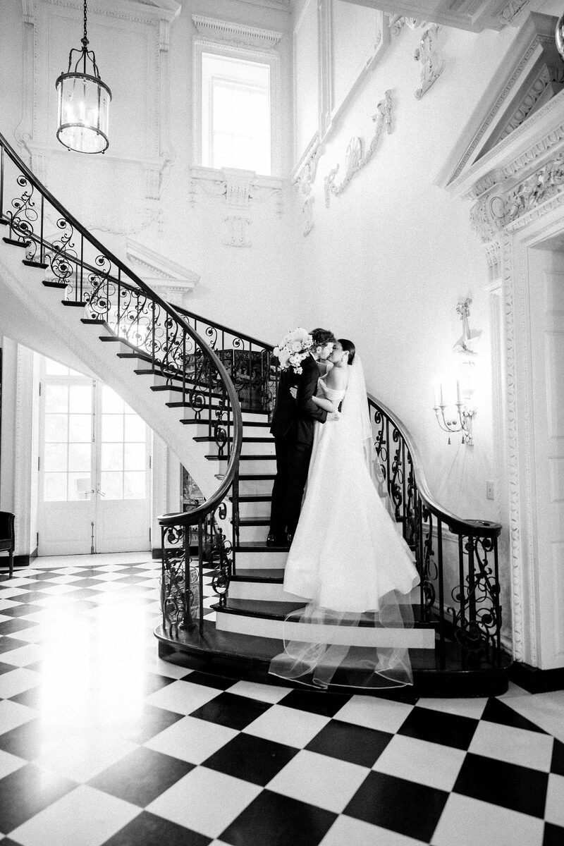 Black and white photo of a bride and groom on a grand spiral staircase