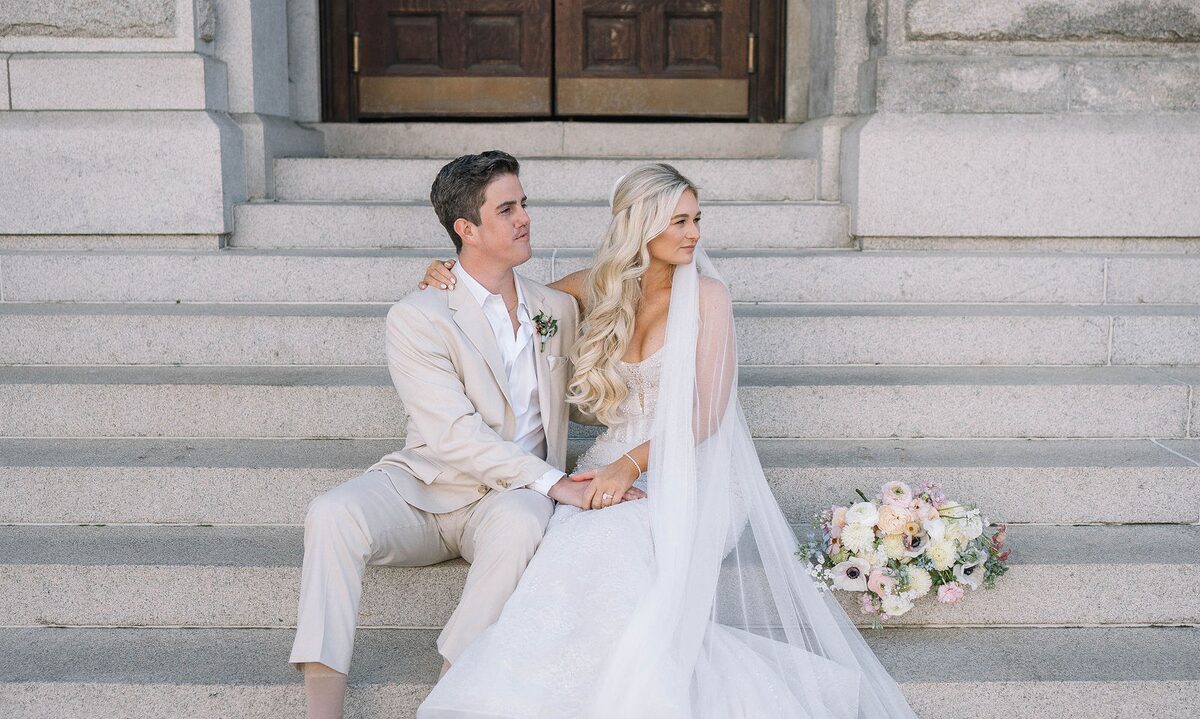 Bride and groom seated on stone steps with her bouquet
