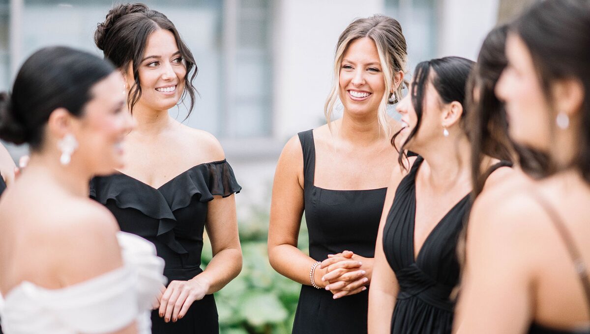 Bridesmaids in black gowns laughing with the bride