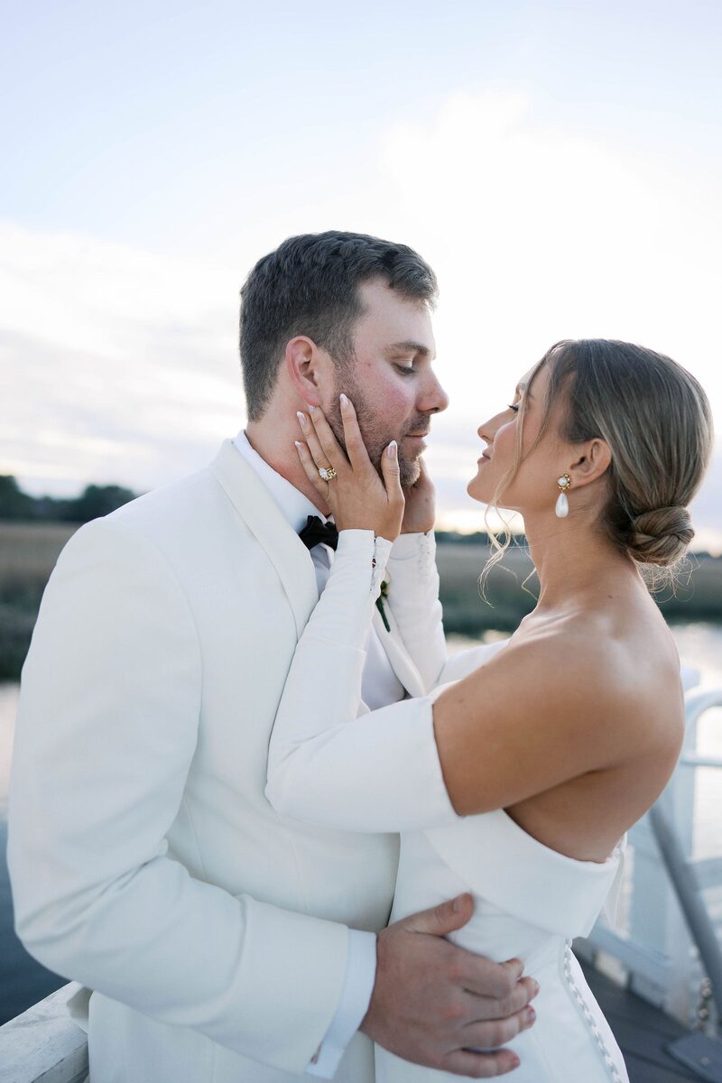 Groom in a white dinner jacket holding his bride close by the water
