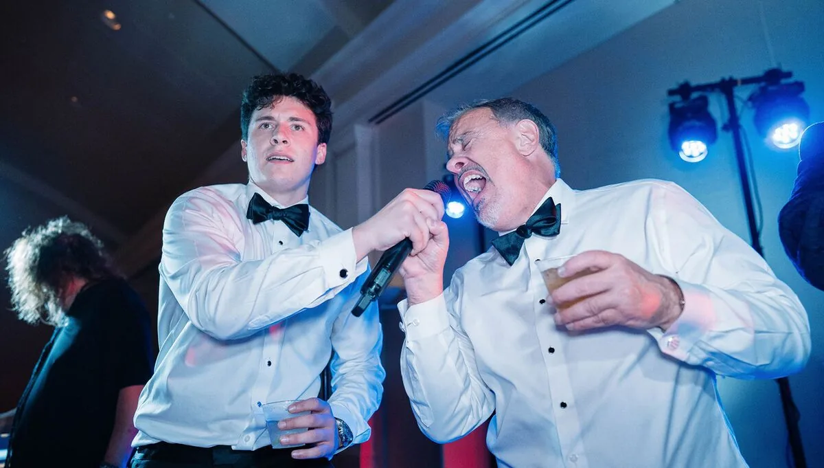 Guests in tuxedos singing into the microphone at a wedding reception