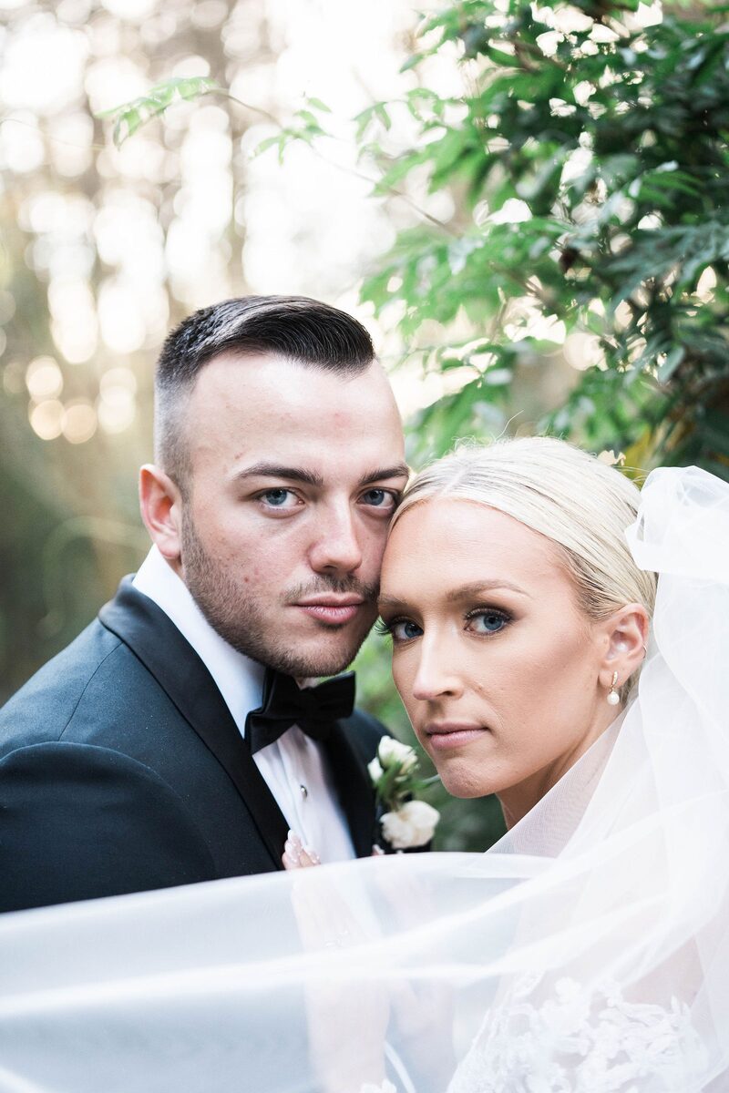 A groom and bride cheek to cheek, her veil lifting in the wind