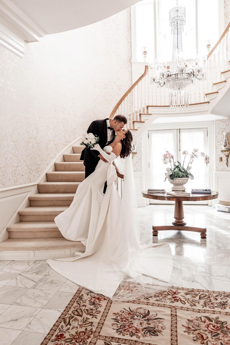 The couple kissing at the foot of a grand staircase