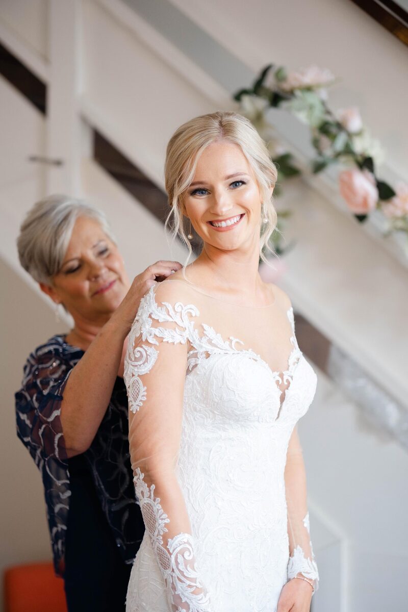 A loved one fastening the bride’s dress at the foot of the stairs