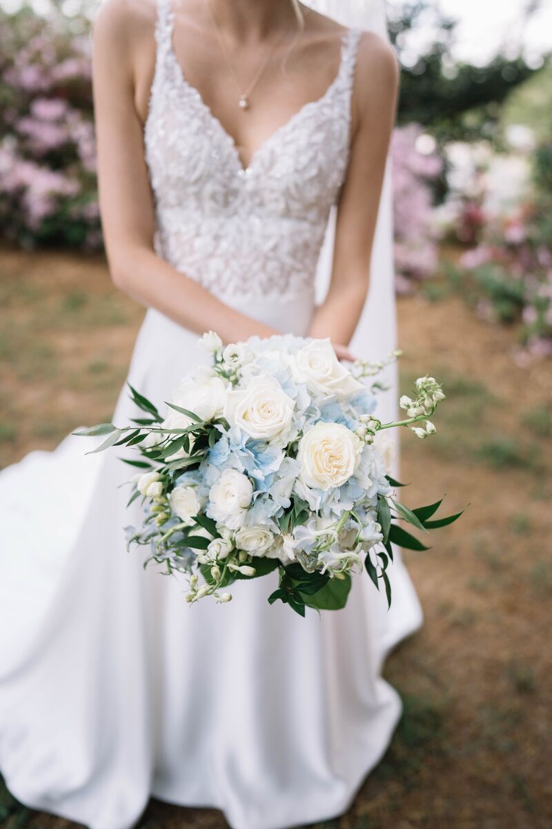Bride holding a white and pale blue bouquet in front of pink azaleas