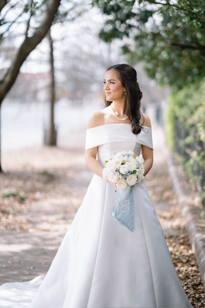 Bridal portrait of a bride in an off-the-shoulder gown with a blue ribbon on her bouquet