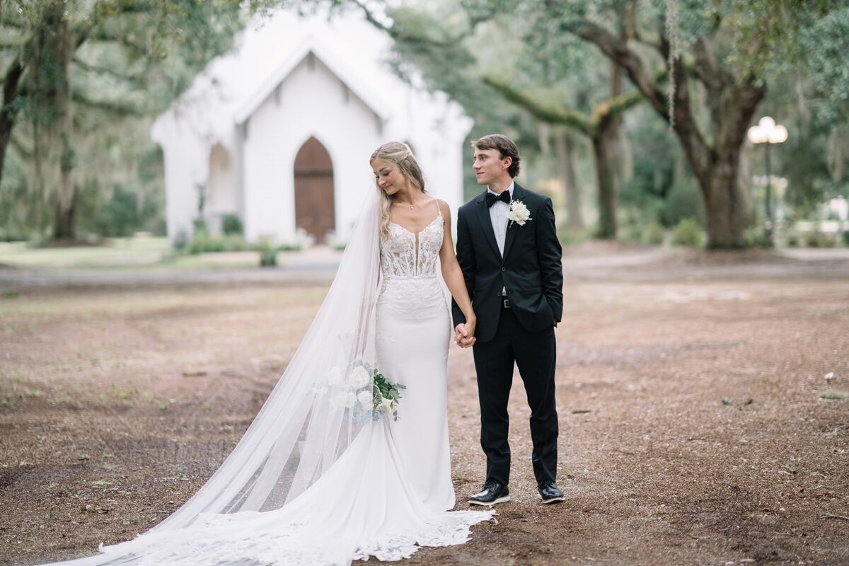 Bride and groom in front of a white chapel beneath live oaks and Spanish moss