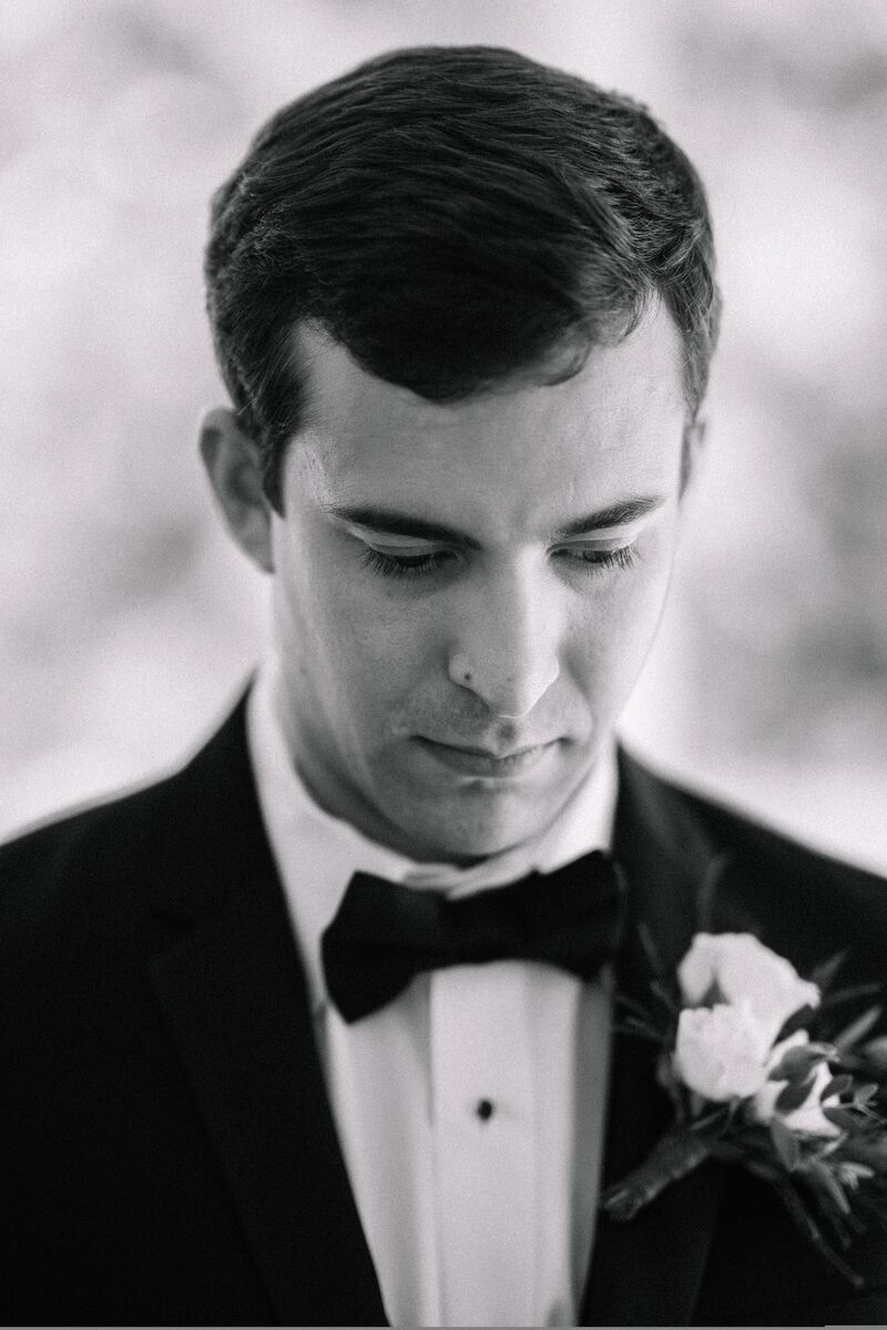 Black and white portrait of a groom looking down at his boutonniere