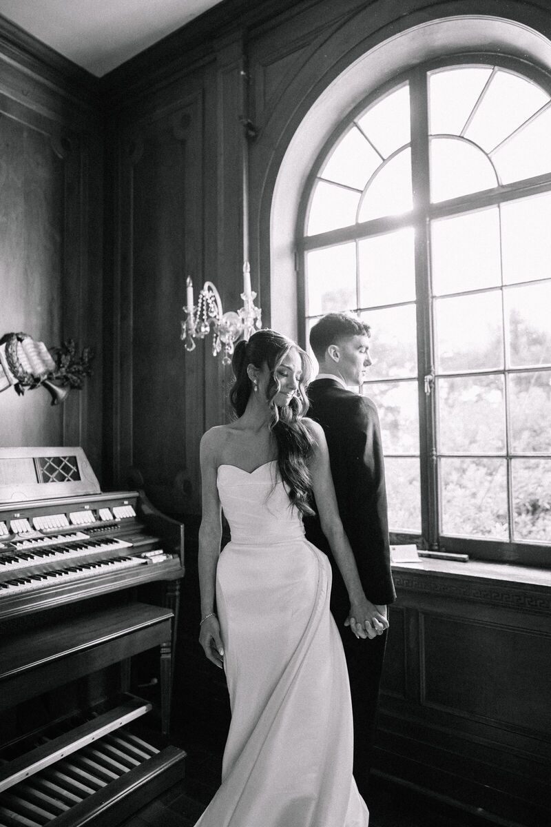 Black and white portrait of a bride and groom by an arched window beside a pipe organ