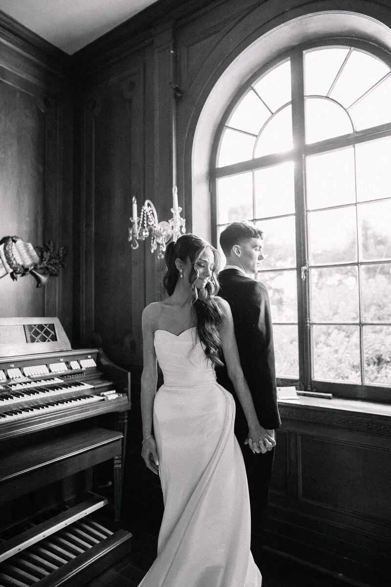 Black and white portrait of a bride and groom by an arched window beside a pipe organ